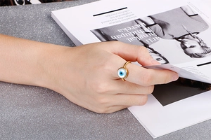 Close-up of golden Evil Eye ring on hand with blue and white enamel detail