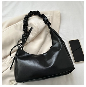 Detail of black hobo bag with trendy scrunchie strap and glossy finish next to a phone