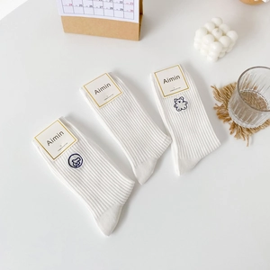 Three pairs of white combed cotton socks with cute cartoon animal embroidery on a desk