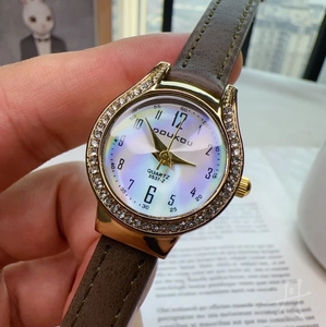 Detail of quartz watch with gold rhinestone bezel and brown leather strap on hand