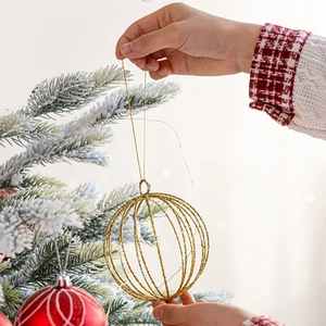 Golden hollow glitter Christmas ball ornament being hung on a frosted Christmas tree branch