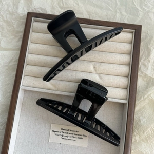Detail showing two black plastic hair claws in matte and glossy finish inside a jewelry box