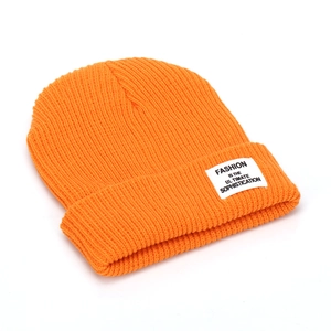 Detail of bright orange ribbed knit beanie with a woven square patch on the folded brim