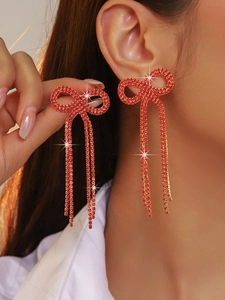 Close-up of red rhinestone bow tassel earrings worn by a model with golden metal finish