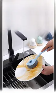Detail of long handle kitchen brush cleaning a greasy plate in a sink effectively
