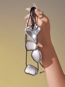 Close-up of polished silver heart and pebble pendants on black cord held by model