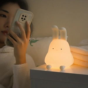 Cute silicone rabbit night light for kids glowing on a bedside table in a cozy bedroom