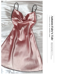 Flat lay detail of pink satin V-neck dress with thin black straps on white silk fabric
