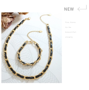 Détail d'un ensemble de bijoux en cuir noir tressé et chaîne dorée avec collier