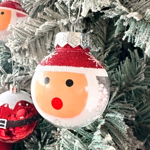 Detail of transparent Santa Claus bauble with snow foam beads and red hat on Xmas tree