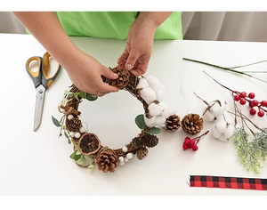 Close-up of hands crafting a DIY Christmas wreath with natural pine cones and cotton buds