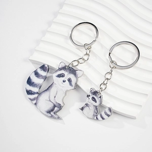 Detail of set of two acrylic raccoon keychains with metal rings on wavy white background