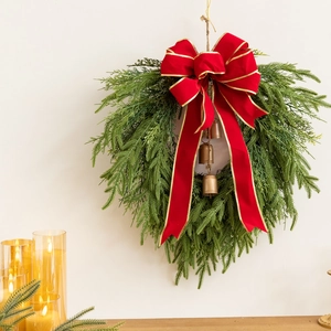 Bohemian Christmas wreath with red velvet bow and brass bells hanging on a white wall