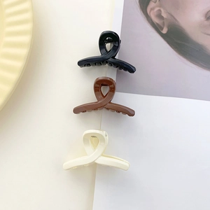 Close-up of matte mini hair claws in black, brown, and cream with crisscross gear design