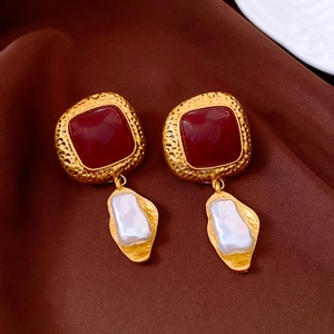 Detail of vintage gold earrings with red resin gems and baroque pearls on brown silk