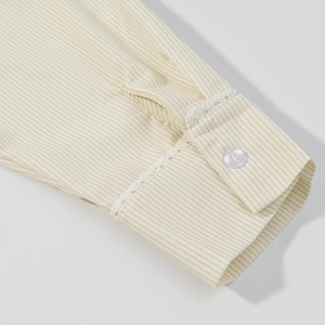 Détail du poignet d'une chemise à rayures jaunes avec dentelle blanche et bouton