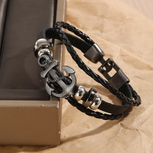 Macro detail of men's black braided leather bracelet with vintage silver anchor charm