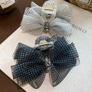 Close-up of mesh bow hair claws with polka dots and rhinestones on a marble textured base