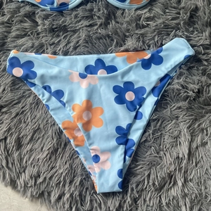 Close-up of light blue bikini bottom with daisy print on a soft grey plush background