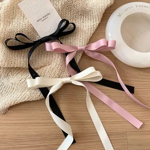 Close-up of elegant long ribbon bow hair clips in black, light pink and cream white silk