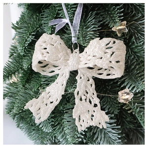 Close-up of white glitter bow ornament with hollow design hanging on a Christmas tree