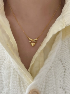 Detail of a dainty golden bow and heart pendant necklace worn on a model's collarbone