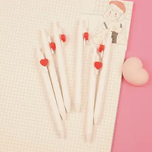 Close-up of cream retractable gel pens featuring red heart clips on a grid notebook