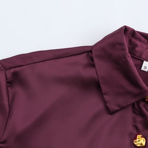 Detailed view of dark burgundy satin shirt with golden embossed buttons and elegant collar