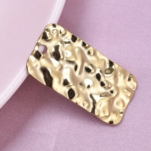 Close-up of a rectangular gold-plated pendant with a hammered texture on purple fabric