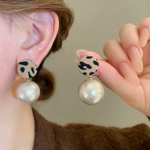 Gros plan sur les clous d'oreilles léopard et perles blanches pour un style automne chic
