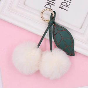 Sweet cherry plush keychain with two white fur balls and golden spring ring on pink surface