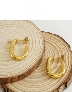 Detailed close-up of chunky gold U-shaped earrings on a rustic wood slice backdrop