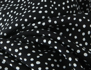 Macro shot of black chiffon fabric with white polka dot patterns and soft drape texture