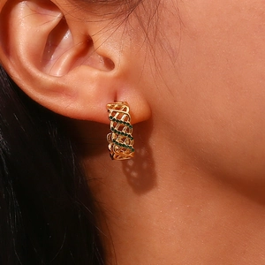Détail macro de boucles d'oreilles dorées en C tissées creuses avec pierres vertes