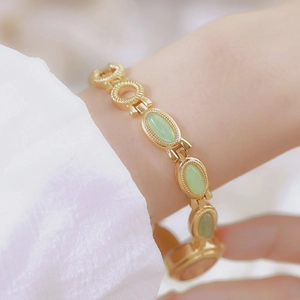 Close-up of gold chain watch with green jade stone inlay on a female wrist