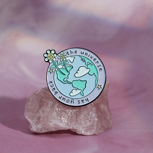 Gros plan d'un badge émaillé Terre circulaire posé sur du quartz rose avec texte motivant