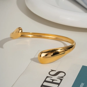 Detail of 18K gold plated wavy open bangle featuring minimalist teardrop ends and mirror finish