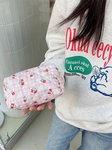 Quilted makeup bag with pink checkered floral pattern held against white tile background