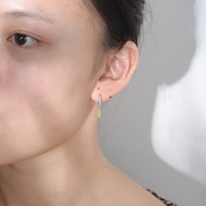 Macro shot of gold feather earrings with turquoise stone worn by model on ear