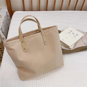 Detail of beige tote bag featuring vertical stripe texture and leather handles with rivets