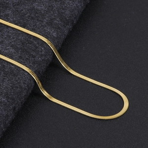 Macro shot of flexible gold plated snake chain necklace with mirror finish on grey fabric