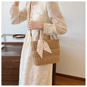 Detail of light brown straw crossbody bag with floral pink scarf and woven strap