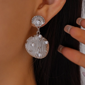 Close-up of shell-shaped silver drop earrings with pearls on a model ear