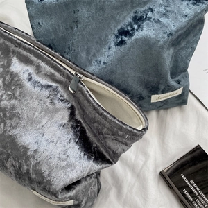 Detail of velvet makeup bags with silver zippers and soft fabric lining shown on a white bed