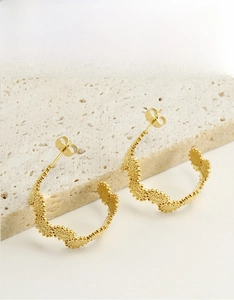 Détail de boucles d'oreilles créoles dorées en acier inoxydable avec relief texturé