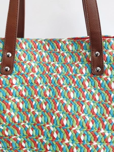 Colorful woven straw tote bag with brown leather handles and silver metal rivets