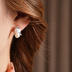 Macro side view of a model wearing the silver flower bud stud earring with a white pearl