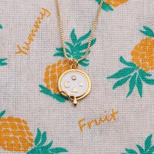 Gold pendant necklace with white enamel celestial snake design on patterned background
