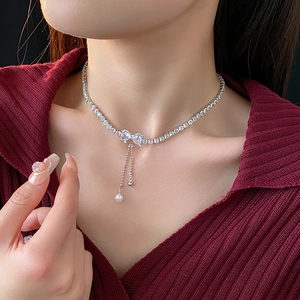 Detail of zircon bowknot pearl tassel necklace worn on a deep red knitted sweater