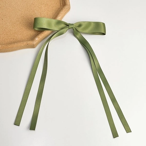 Detail of avocado green satin bow hair clip featuring long flowing silk ribbons